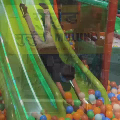 Children of various ages enjoy a vibrant indoor play zone filled with colorful ball pits, slides, and climbing structures. The atmosphere is lively and fun, with kids actively engaged in play and a birthday celebration in progress. A "Hot Wheels" themed birthday banner and jungle-themed decor add to the festive environment.