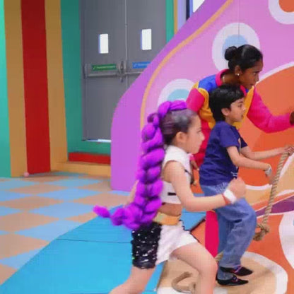 Children of various ages enjoy a vibrant indoor play area filled with colorful slides, climbing walls, and arcade games. The atmosphere is lively and energetic, with kids actively engaged in climbing, sliding, and playing. The environment features bright, playful decor and exciting attractions like VR simulators and air hockey tables.