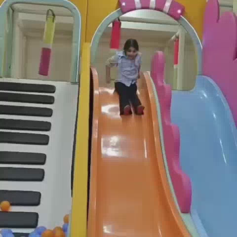 Children of various ages enjoy a vibrant indoor play area, sliding down colorful slides into ball pits, bouncing on trampolines, and climbing a rock wall. The atmosphere is lively and playful, with bright decorations and a sense of joyful exploration.