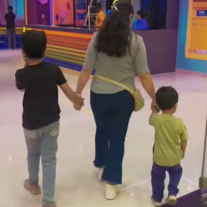 Children and adults enjoy a vibrant indoor trampoline park filled with colorful foam pits, slides, and climbing walls. The atmosphere is energetic and playful, with people of various ages bouncing, climbing, and sliding. The park features bright neon lights and a lively, fun-filled environment.