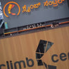Young adults and children are enjoying a thrilling indoor rock-climbing experience at a vibrant climbing center. The colorful walls are equipped with various holds, and participants are safely harnessed, ready to ascend. The atmosphere is energetic and adventurous, with people of different ages participating.