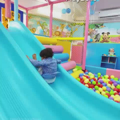 Children of various ages enjoy a vibrant indoor play zone filled with colorful slides, ball pits, climbing walls, and interactive games. The atmosphere is lively and fun, with kids actively engaged in playful activities. The play area features soft, padded surfaces and bright, cartoon-themed decorations, creating a safe and stimulating environment for young children.