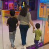 A family enjoys a vibrant indoor trampoline park with colorful foam pits, climbing walls, and slides. Children and adults alike leap and play in the energetic atmosphere, surrounded by neon lights and playful decor.
