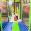 Children of various ages enjoy a vibrant indoor playground filled with colorful slides, a ball pit, and a zip line. The atmosphere is lively and energetic as kids navigate the soft play structures and engage in playful activities.