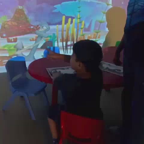 Children engage in interactive digital games and physical activities at a vibrant indoor play park. The setting features projected underwater scenes, a ball pit, trampolines, and a dinosaur-themed area, creating a lively and exciting atmosphere for young visitors.