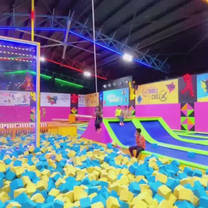 This video showcases a vibrant indoor amusement park filled with colorful trampolines, foam pits, and inflatable slides. People of various ages are seen enjoying thrilling activities like jumping, swinging, and sliding. The atmosphere is energetic and fun, with bright neon lights and playful decorations creating an exciting environment.