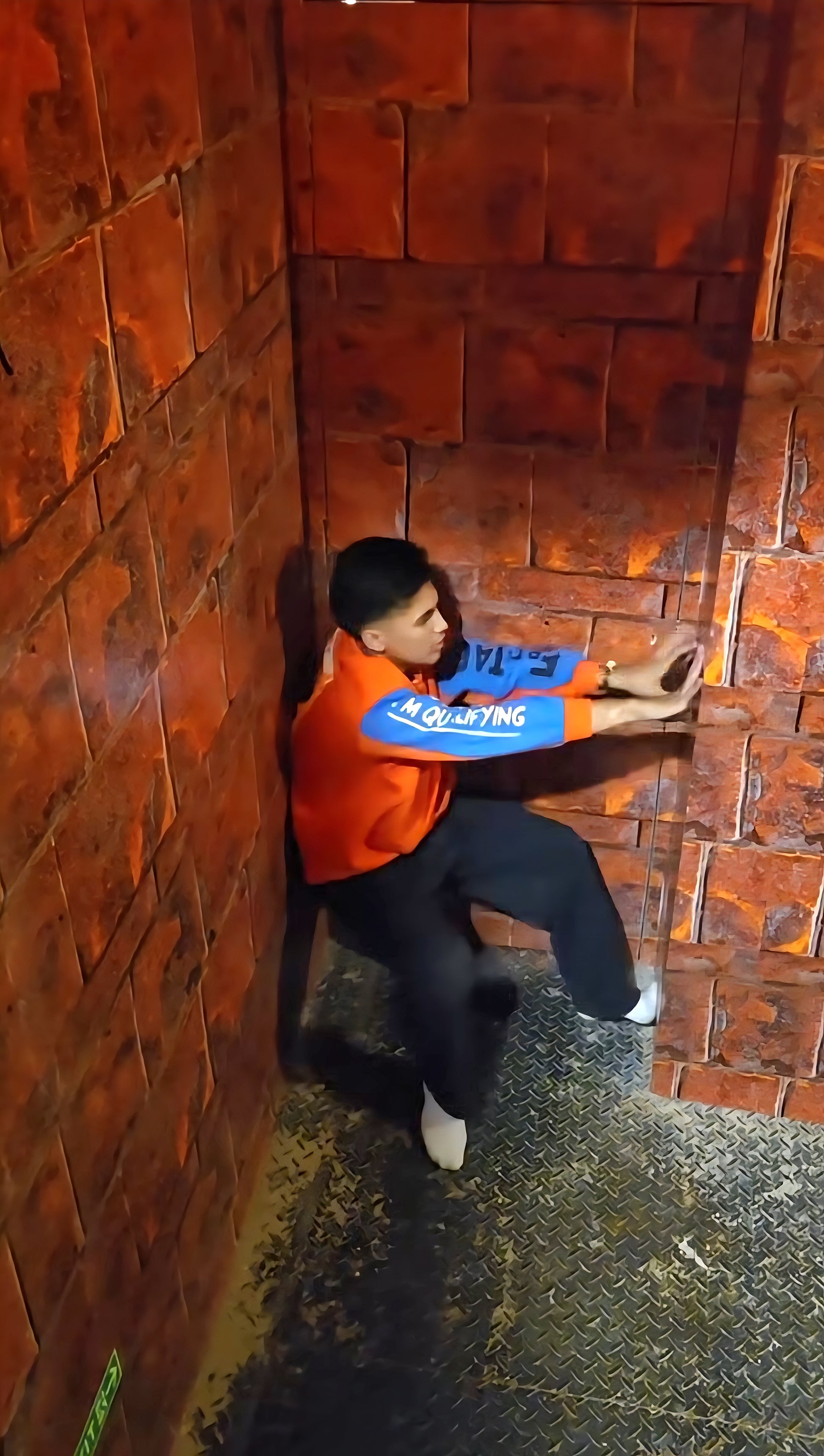 Young man in orange and blue jacket balancing against textured brick walls in Rajinder Nagar escape room setting
