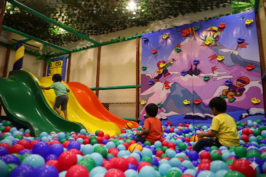 Children playing in a colorful ball pit with slides and a mural in the background.