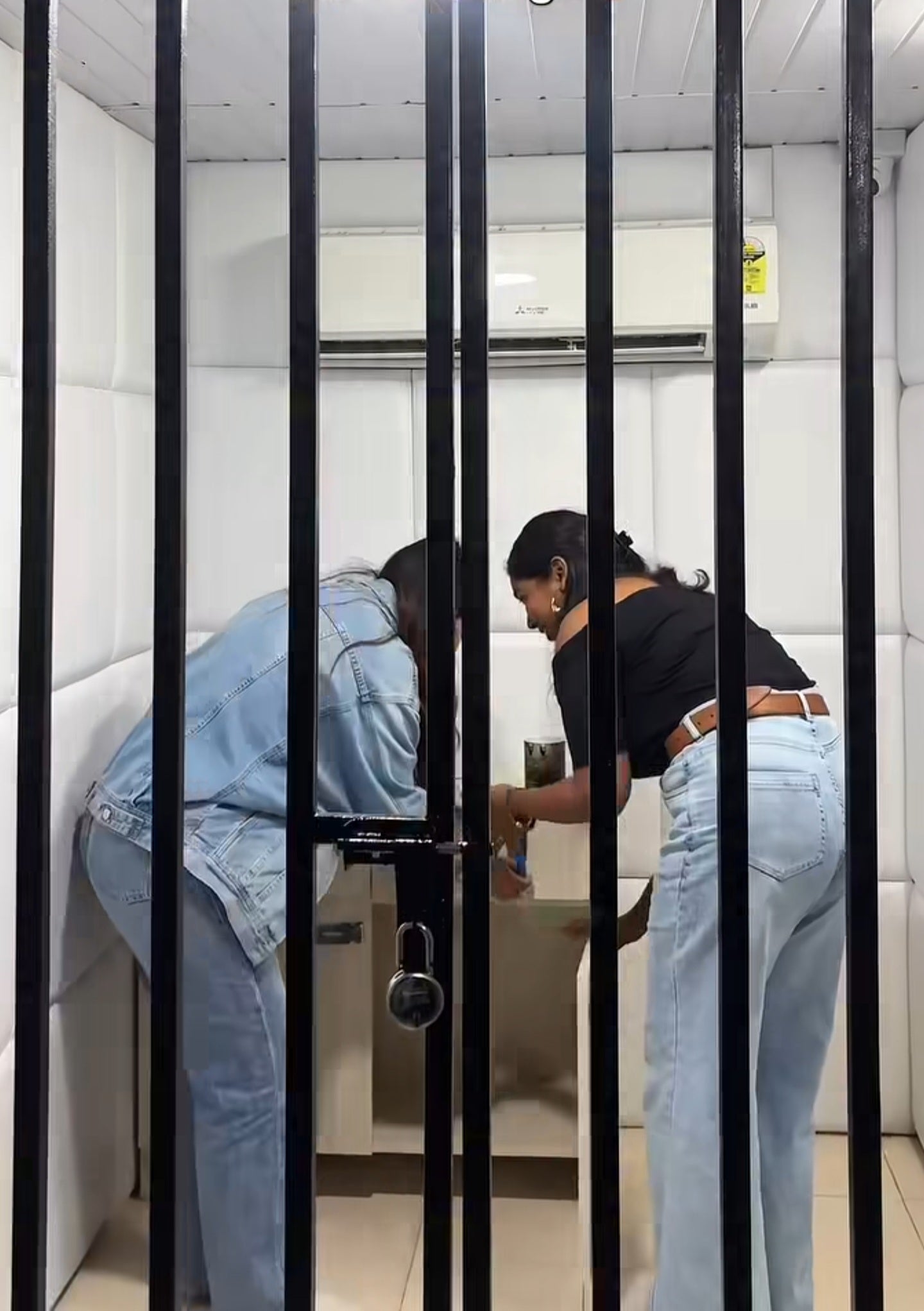 Two women working together to solve a puzzle inside a white padded escape room at Rajinder Nagar location
