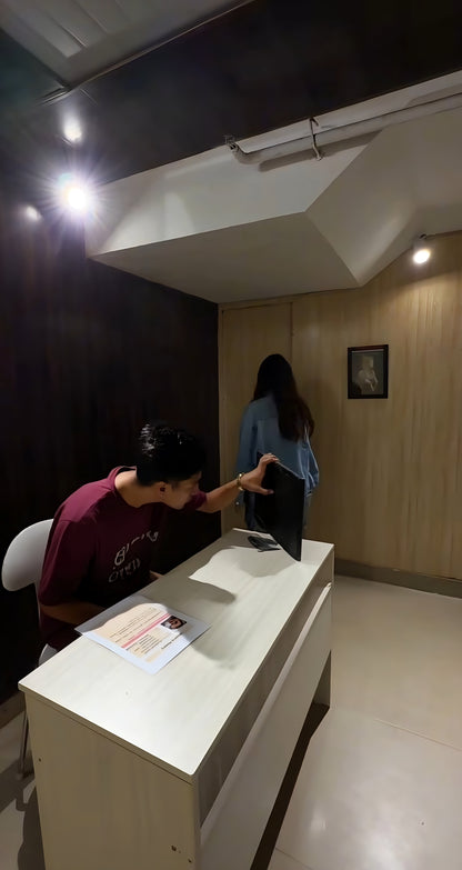 Person sitting at desk looking at monitor while woman walks toward wooden wall with framed picture in dim room