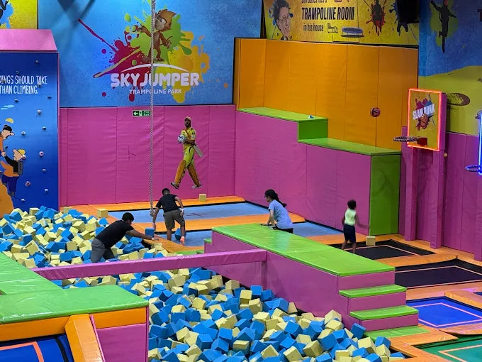 Children playing in a colorful indoor trampoline park with various activities and safety padding.
