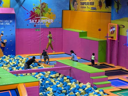 Children playing in a colorful indoor trampoline park with various activities and safety padding.