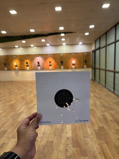 A person holds a target with several bullet holes at a shooting range.